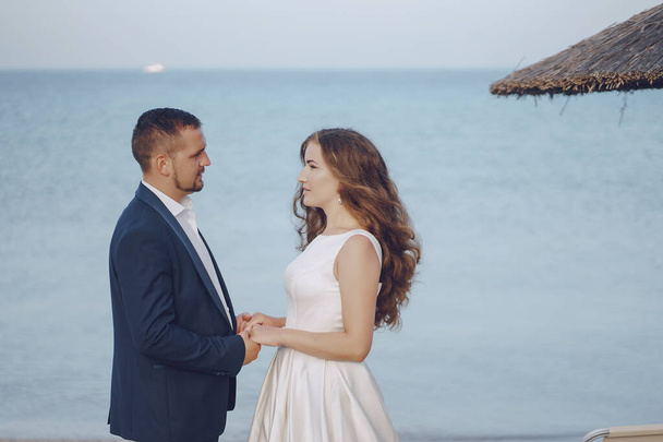 beautiful young long-haired bride in white dress with her young husband on the beach - Φωτογραφία, εικόνα