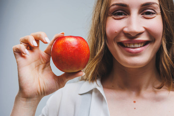 Cute brunette woman in white shirt holding red apple in hand standing on isolated white background dietetics and nutrition. Healthy food - Foto, immagini