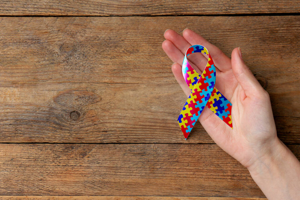 Día Mundial del Autismo. Mujer con cinta de rompecabezas de colores sobre fondo de madera, vista superior con espacio para el texto - Foto, Imagen