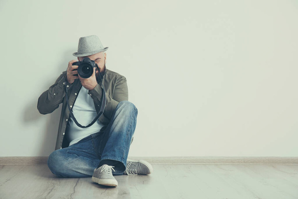 Professional photographer with camera on floor near white wall. Space for text - Zdjęcie, obraz