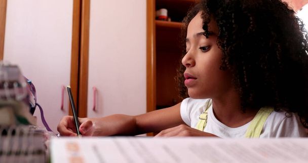 Смешанная расистка пишет заметки, делая домашнее задание. Девочка сосредоточилась на учебе. - Фото, изображение