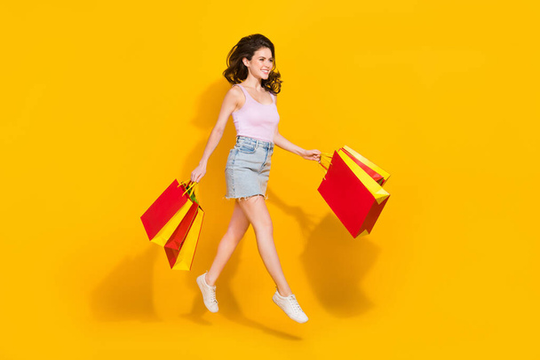 Full length photo of pretty shiny lady dressed pink singlet walking jumping high holding bags isolated yellow color background. - Photo, Image