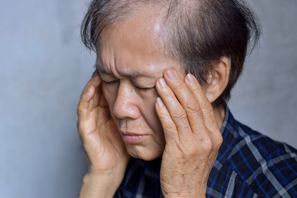 Asian elder man massaging his temple. Concept of eye pain, strain or cluster headache. - Photo, image