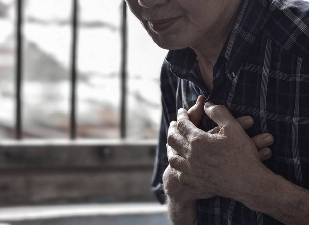 Asian elder man suffering from central chest pain. Chest pain can be caused by heart attack, myocardial infarct or ischemia, myocarditis, pneumonia, stress, etc. - Photo, Image