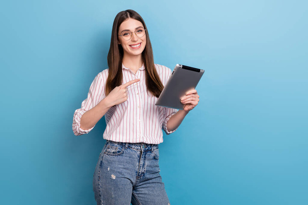 Portrait of beautiful cheerful brown haired girl demonstrating ebook isolated over bright blue color background. - Foto, Imagen