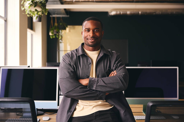 Sorrindo jovem preto masculino em pé no escritório olhando para a câmera com braços cruzados - Foto, Imagem