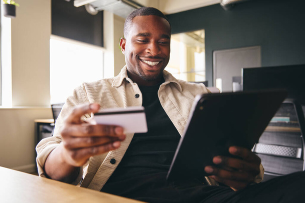 Uomo sorridente che effettua il pagamento online su tablet che detiene carta di credito - Foto, immagini