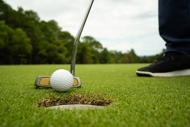 Golfer legt Ball auf dem grünen Golf, Linsenschlag bei Sonnenuntergang abends. Golfbälle, die von Golfern auf dem Green-Grass-Golfplatz bei Sonnenuntergang gelocht werden. - Foto, Bild