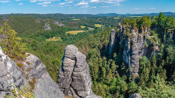 Panorámica sobre pilares monumentales de piedra arenisca Bastei, formación de rocas y montones rodeados de bosques antiguos en la aldea Kurort Rathen en el parque nacional Sajón Suiza por Dresde, Sajonia, Alemania - Foto, Imagen