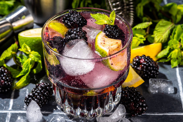 Blackberry lemonade or mojito with lime, and mint. Iced fresh summer cocktail with whole and smashed blackberries, lime, miint and ice cubes. Dark tiled background copy space - Foto, Bild