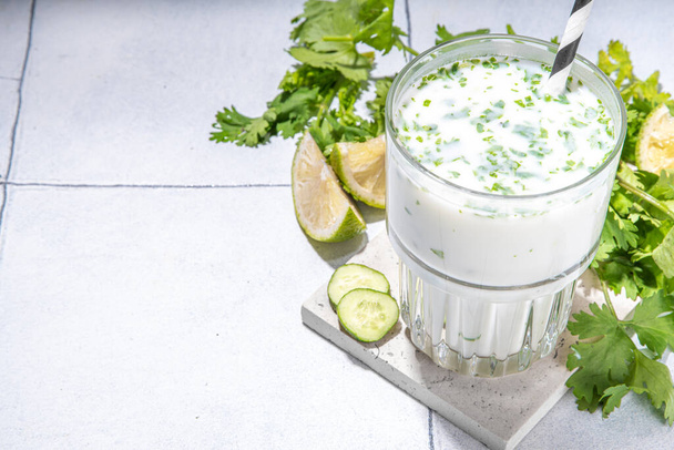 Fresh asian yogurt drink kefir, ayran in glass with smashed herbs. Ayran, homemade summer healthy cocktail  with herbs, lime, cucumbers. Probiotic, postbiotic fermented dairy drink - Φωτογραφία, εικόνα
