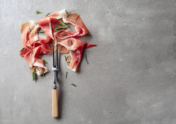 Prosciutto with rosemary on an old concrete background. Traditional Mediterranean snack. Copy space. - Fotó, kép