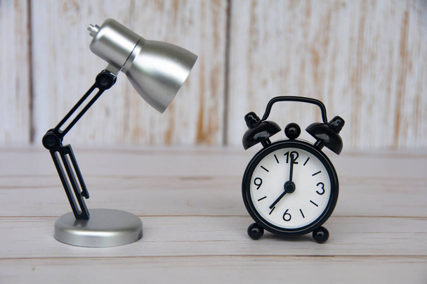 Reloj despertador apuntando a las 7 en punto con lámpara de mesa sobre fondo de madera. Copiar espacio y tiempo concepto - Foto, imagen