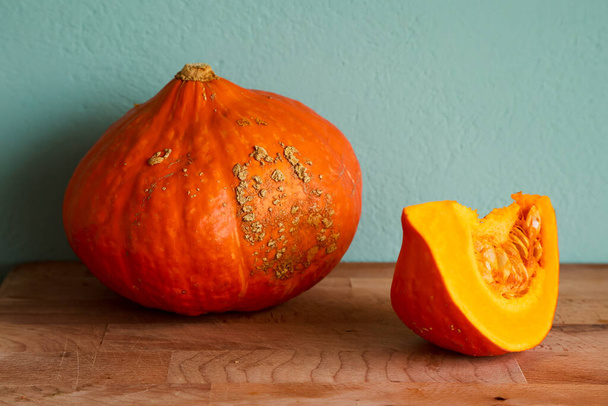 Vivid orange Hokkaido pumpkin with selective focus on wooden plake against blurred blue green turquoise stucco wall background. Autumn vegetables in interior closeup. - Foto, immagini