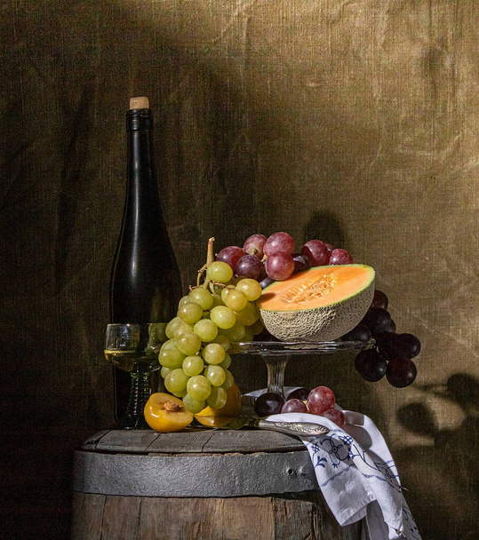 still life of fruit and wine standing on an old wine barrel in a dark basement - 写真・画像
