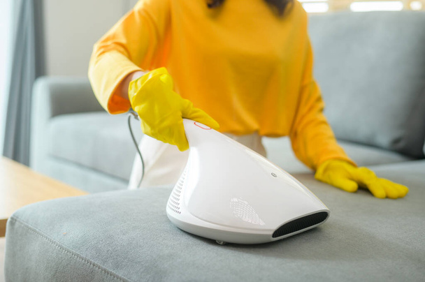 Young happy woman wearing yellow gloves  and vacuum Cleaning a sofa in living room. - Photo, Image
