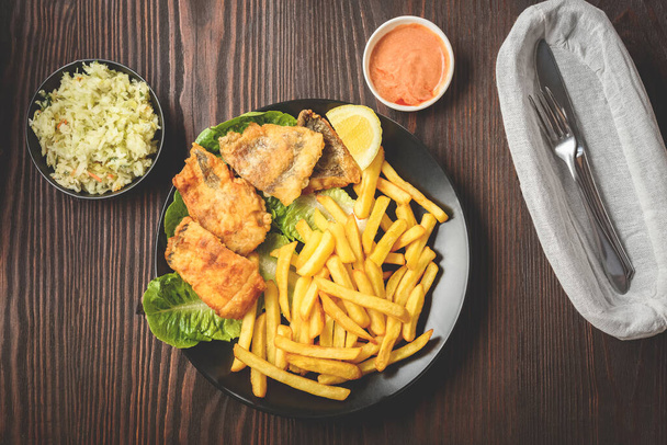 fish and chips on a black plate, served with salad and sauce - Фото, изображение