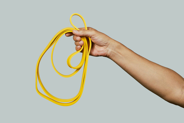 closeup of a man with a yellow resistance band in his hand, on a pale gray background - Foto, Imagem