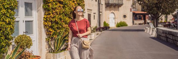 BANNER, LONG FORMAT Woman tourist enjoying Colorful street in Old town of Perast on a sunny day, Montenegro. Travel to Montenegro concept. Scenic panorama view of the historic town of Perast at famous - Фото, изображение