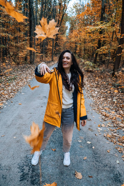 Happy brunette woman holding yellow maple autumn leaves in fall park. Portrait of cheerful young woman with autumn leaves - Photo, Image