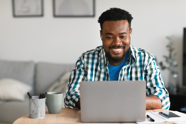 Cheerful Black Man Using Laptop Working Distantly Online Sitting At Desk At Home. Freelancer Guy Browsing Internet. Freelance Career And Remote Job, Technology Concept - Foto, Imagem