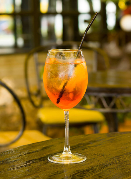 Glass of cold aperol spritz with ice cubes, orange slice and cocktail straw. A glass of refreshing cocktail on a wooden table in a restaurant - Photo, Image