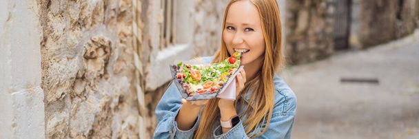 BANNER, LONG FORMAT Young woman tourist eating traditional pizza in the old town of Budva. Travel to Montenegro concept. - Foto, afbeelding