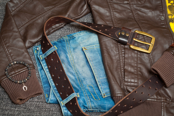 Коричнева шкіряна куртка, джинси з поясом, сорочка і браслет на руці
 - Фото, зображення