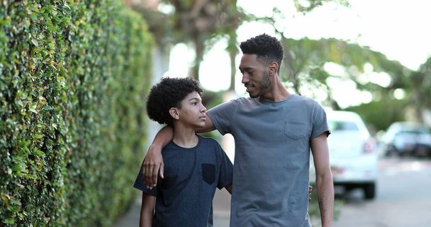 Two brothers walking together in sidewalk. Black brother giving advice to younger sibling - Photo, image