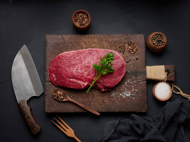 Raw beef tenderloin lies on a brown wooden board, black table. View from above - Photo, Image