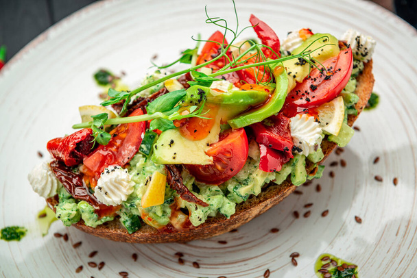 Bruschetta with sun-dried tomatoes, cream cheese, avocado and fresh vegetables. Healthy and wholesome food. Serving food in a restaurant. Photo for the menu. - Foto, Bild