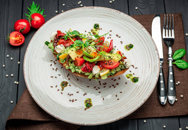 Bruschetta with sun-dried tomatoes, cream cheese, avocado and fresh vegetables. Healthy and wholesome food. Serving food in a restaurant. Photo for the menu. - Foto, afbeelding