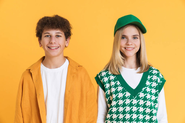 White two teenagers smiling at camera while posing together isolated over yellow wall - Φωτογραφία, εικόνα