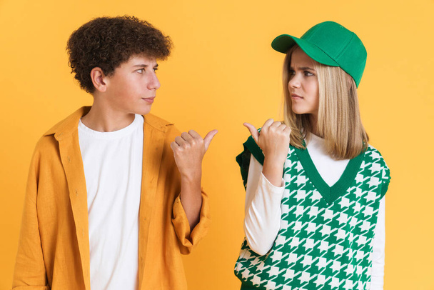 White girl and boy frowning while pointing fingers at each other isolated over yellow background - Foto, immagini