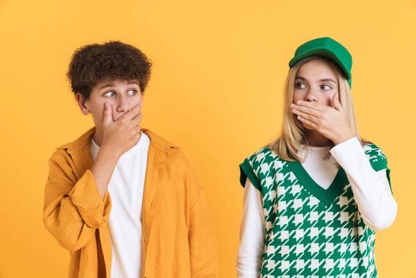 White girl and boy expressing surprise while covering their mouths isolated over yellow background - Φωτογραφία, εικόνα