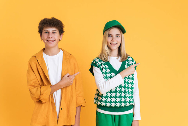 White girl and boy smiling while pointing fingers aside isolated over yellow background - Foto, immagini