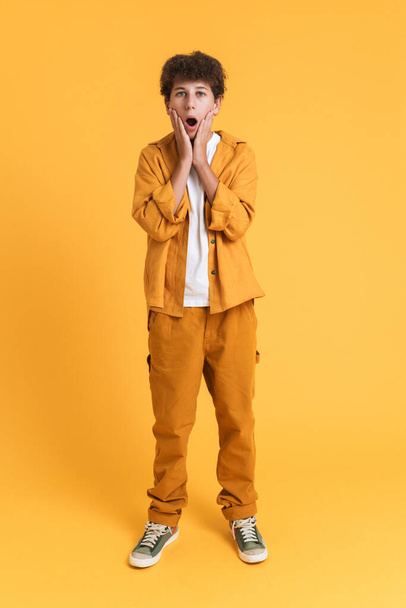 White boy wearing suit expressing surprise at camera isolated over yellow background - Fotó, kép