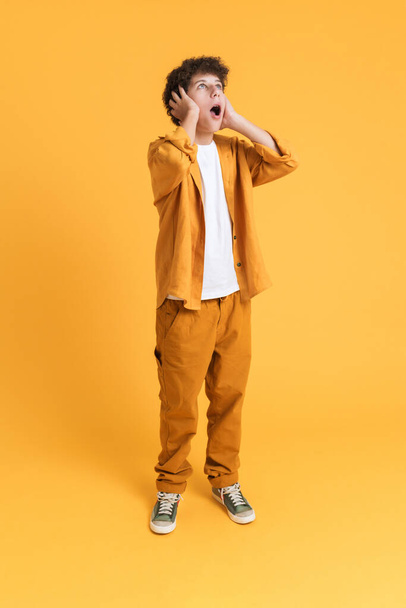 White boy wearing suit expressing surprise and looking upward isolated over yellow background - Foto, Imagem
