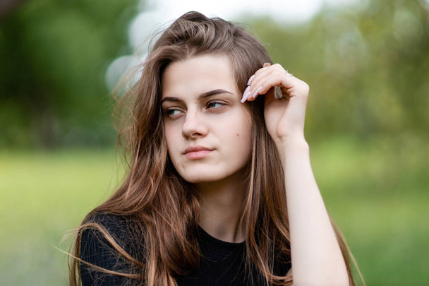 young and beautiful girl with long hair wearing a black t-shirt on a green background looks to the side. - Foto, immagini