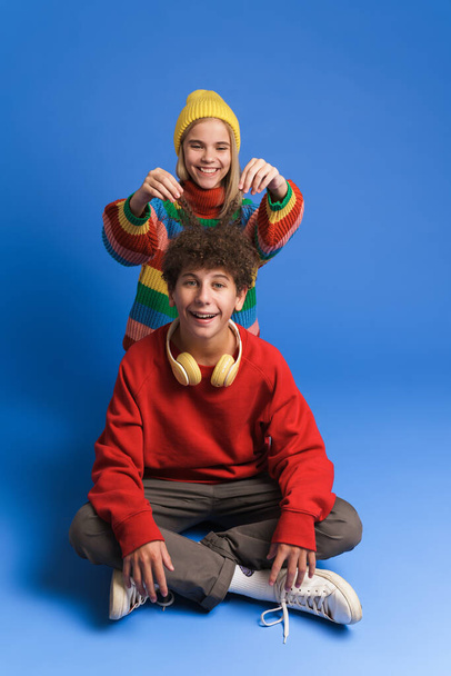 White two teenagers laughing while making together isolated over blue wall - Foto, immagini