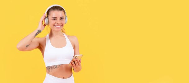 szczęśliwy sport kobieta ze słuchawkami i smartfon na żółtym tle. Kobieta odizolowana twarz portret, baner z makietą przestrzeń copyspace - Zdjęcie, obraz
