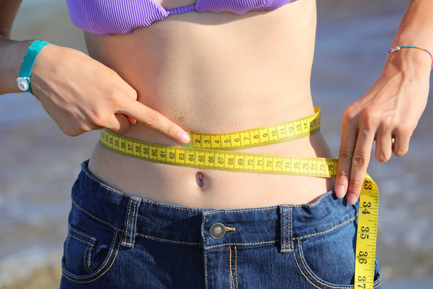 thin girl who measures her waist with the flexible measuring tape and shows her navel on her belly - Photo, Image