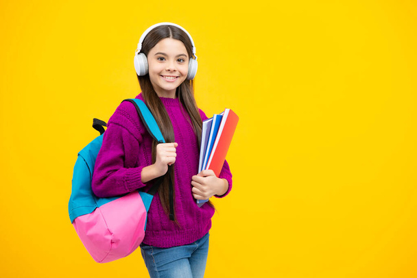 Vissza a suliba. Tinédzser iskolás lány hátizsákkal és fejhallgatóval könyveket tart készen a tanulásra. Iskolás gyerekek elszigetelt sárga stúdió háttér - Fotó, kép