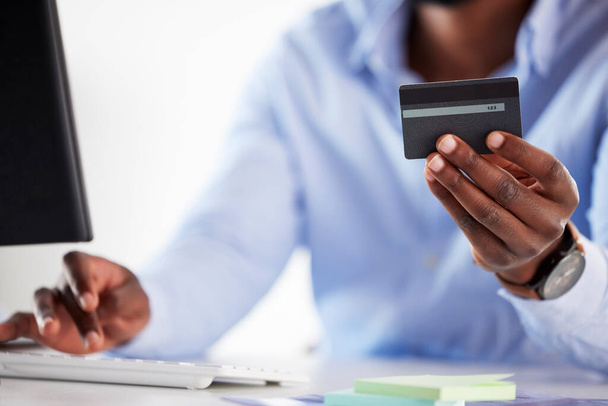 Close-up van een Afro-Amerikaanse zakenman die online geld uitgeeft met een creditcard en computer in een kantoor. Het maken van aankoop transactie met beveiligde bancaire betaling. Begroting financiering voor rekeningen en - Foto, afbeelding