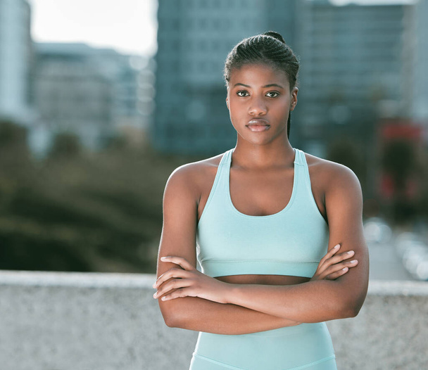 Portrait of one serious young african american woman standing with arms crossed ready for exercise outdoors. Determined female athlete looking focused and motivated for training workout in the city. - Zdjęcie, obraz