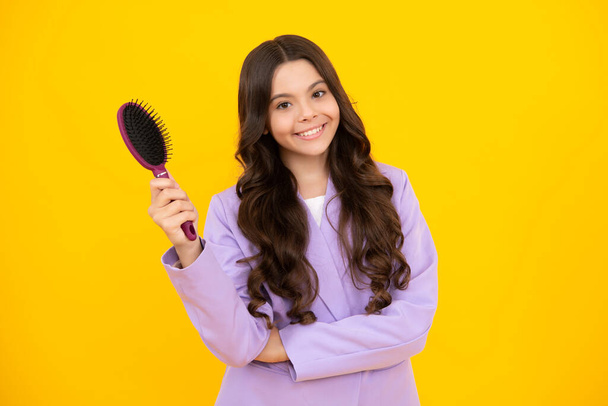 Teenager brushing combing hair with big comb on yellow isolated studio background. Teen girl with hairbrush. Kids hairstyle. Happy positive and smiling emotions of teenager girl - Foto, imagen