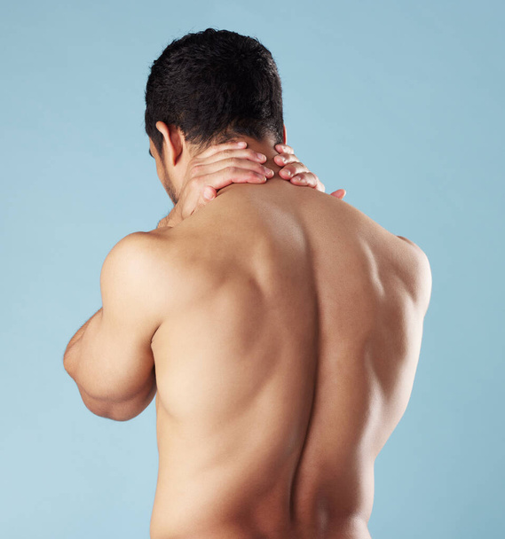 Rearview young mixed race man standing shirtless in studio isolated against a blue background. Unrecognizable topless male athlete suffering from back pain or ache. Hes picked up a fitness injury. - Photo, Image