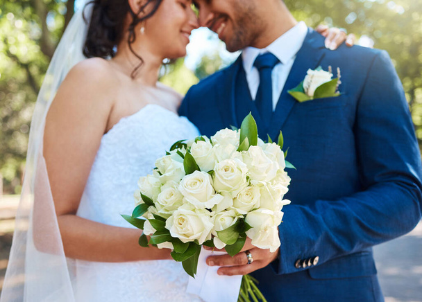 Close up of a bride in her wedding dress and groom in suit holding on to a bouquet while standing together on their wedding day. Couple tying the knot. Wedding detail. - Foto, imagen