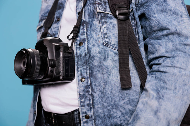 Крупный план энтузиаста фотографии с профессиональной камерой DSLR, стоящей на синем фоне. Фотограф в джинсовой куртке и с современным фотоустройством - Фото, изображение