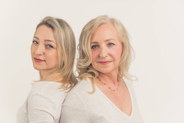 Caucasian beautiful middle-aged calm women standing back to back, touching their faces, looking at the camera. Studio shot. High quality photo - Fotoğraf, Görsel